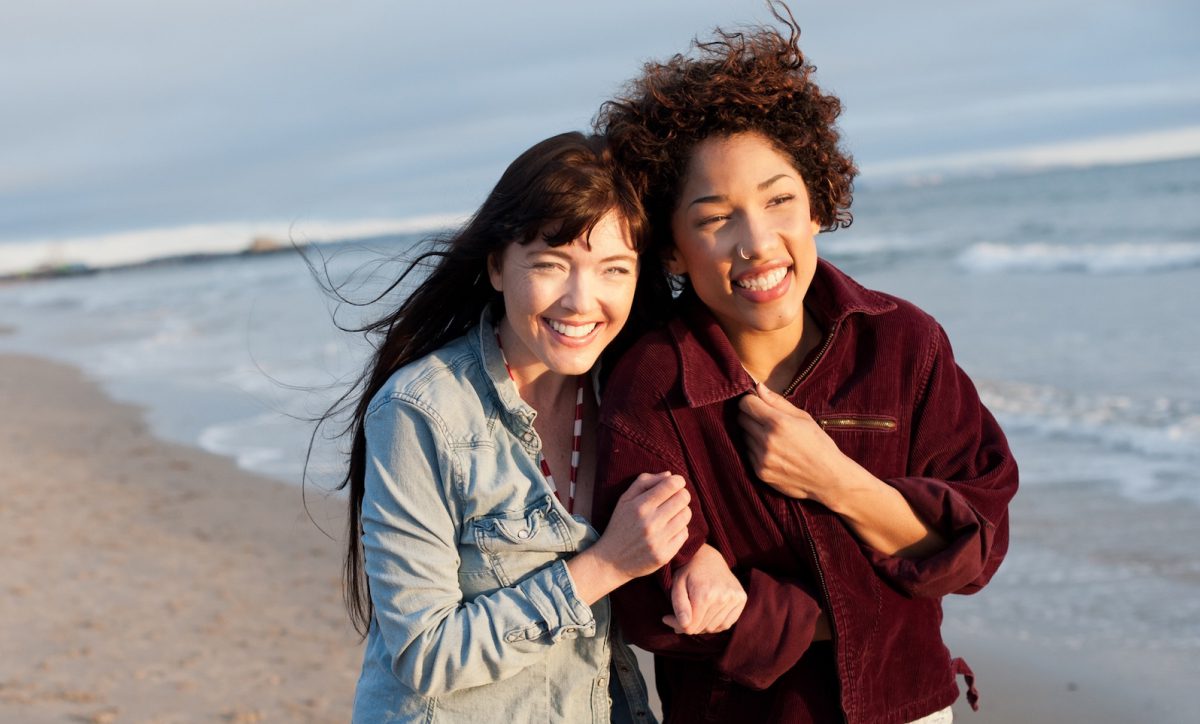 A family of four sits together on a couch, with a young child nestled between them, smiling and enjoying their time.